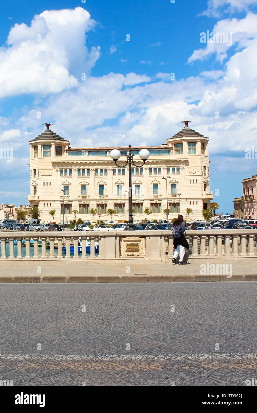Syracuse, Sicily, Italy - Apr 10th 2019: Male tourist photographer standing on bridge and taking picture of beautiful harbor on sunny day. The bridge is connecting Syracuse and famous Ortigia Island. Stock Photo