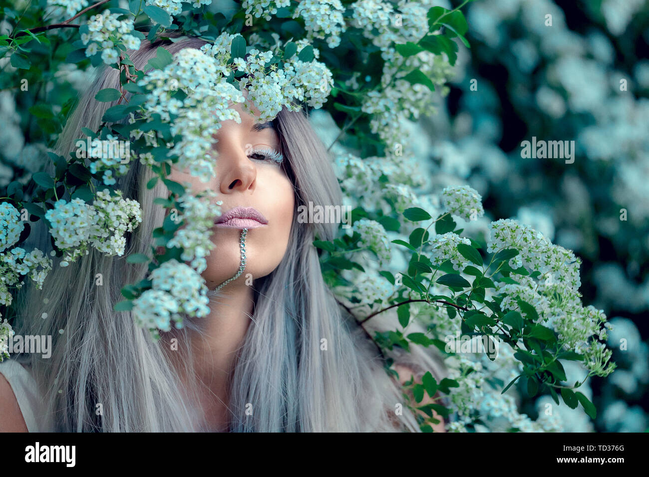 Fairy-tail forest nymph, beautiful sexy woman with white hair at spring garden, sitting on blooming tree, vintage dreamy fashion style Stock Photo