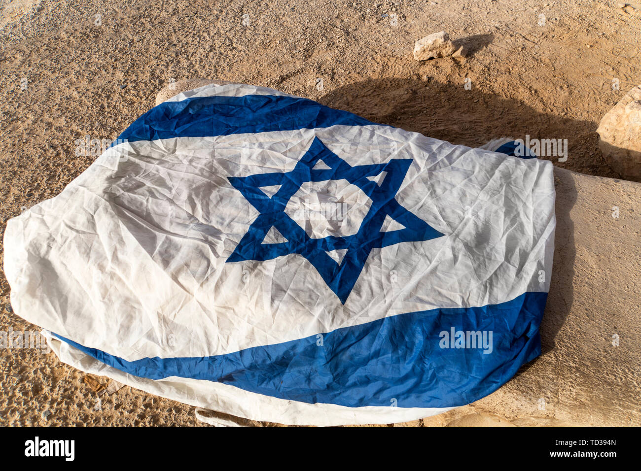 Close up of white and blue flag with David's star left on the ground in arid place. Symbol of promised land. Patriotic feelings. Protecting Israel Stock Photo