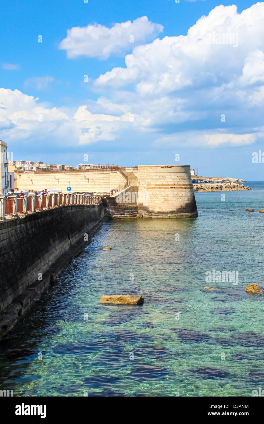 Vertical picture of clear sea and nearby city coast of Sicilian Syracuse, Italy. Taken near the historical center in Ortigia Island. Sunny day, blue sky with clouds. Popular tourist destination. Stock Photo