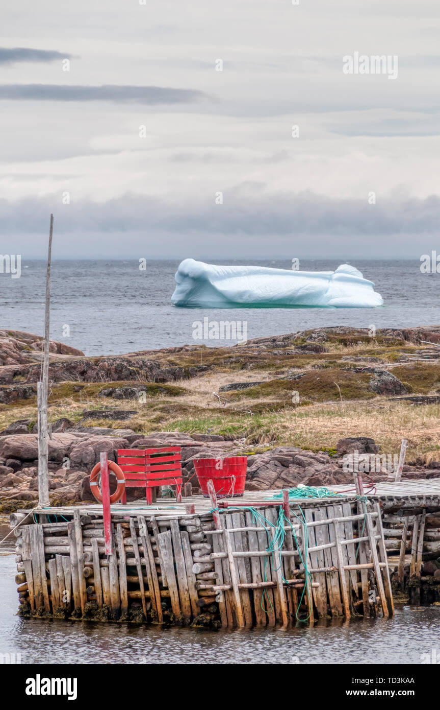 An iceberg floats past a jetty at the small Labrador town of West Saint Modeste in the late afternoon. Stock Photo