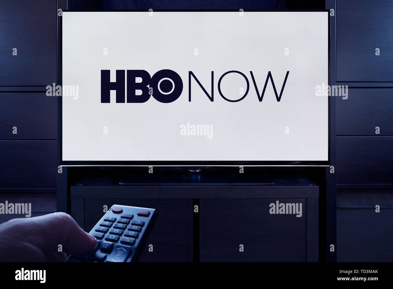 A man points a TV remote at the television which displays the logo for the HBO Now on demand video streaming service (Editorial use only). Stock Photo