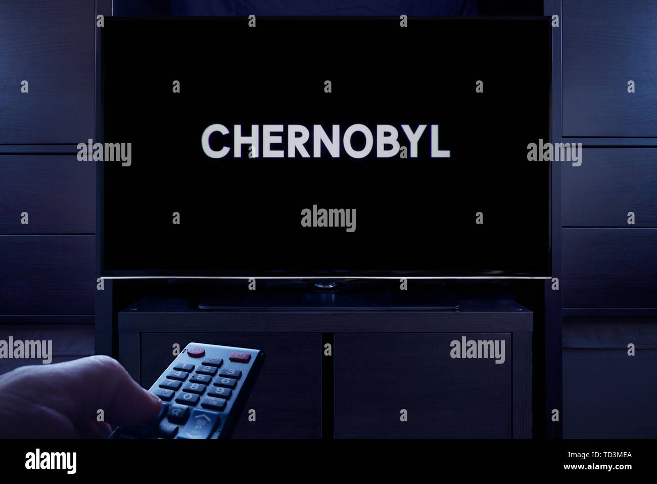 A man points a TV remote at the television which displays the Chernobyl main title screen (Editorial use only). Stock Photo