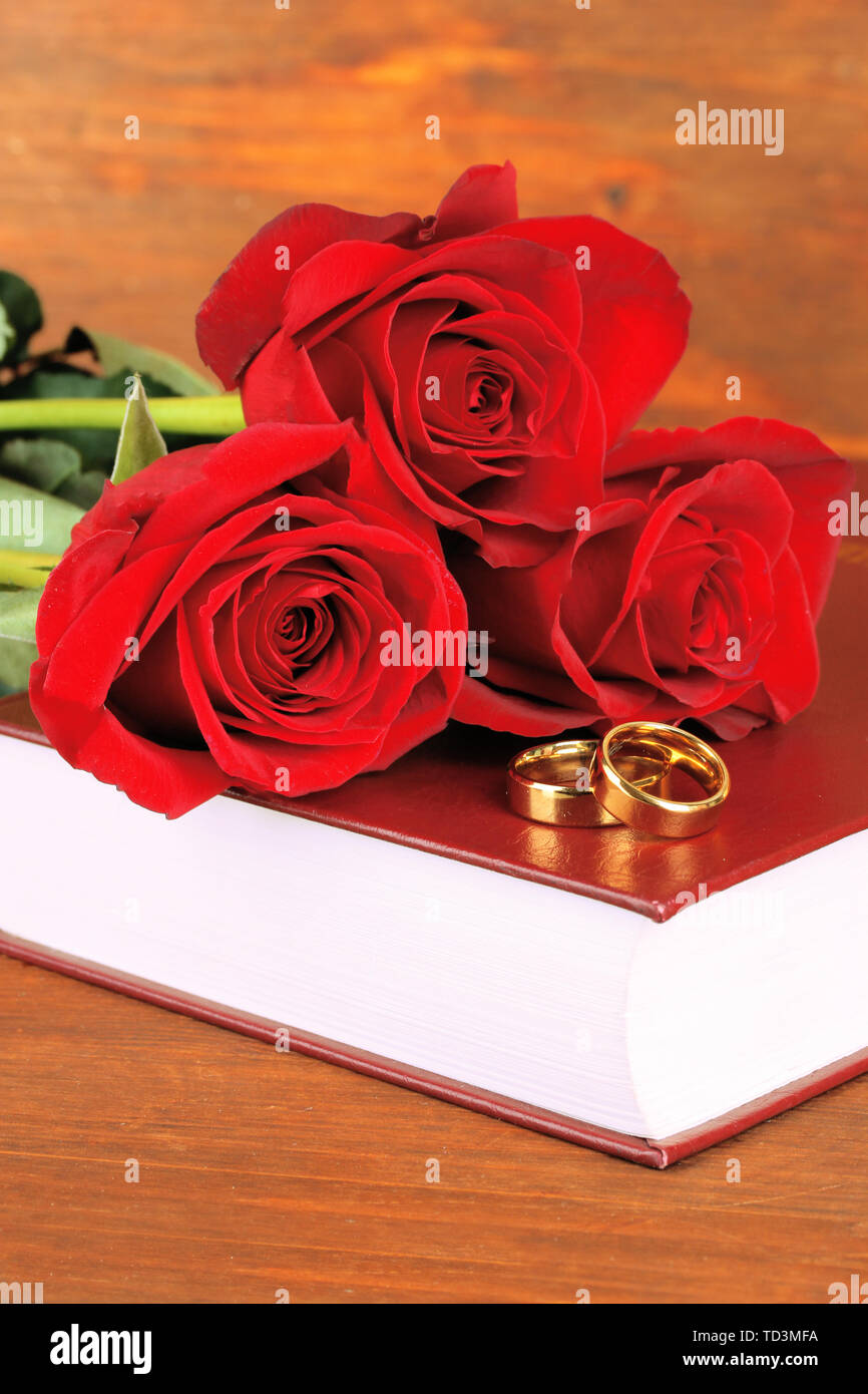 Wedding rings on bible with roses on wooden background Stock Photo