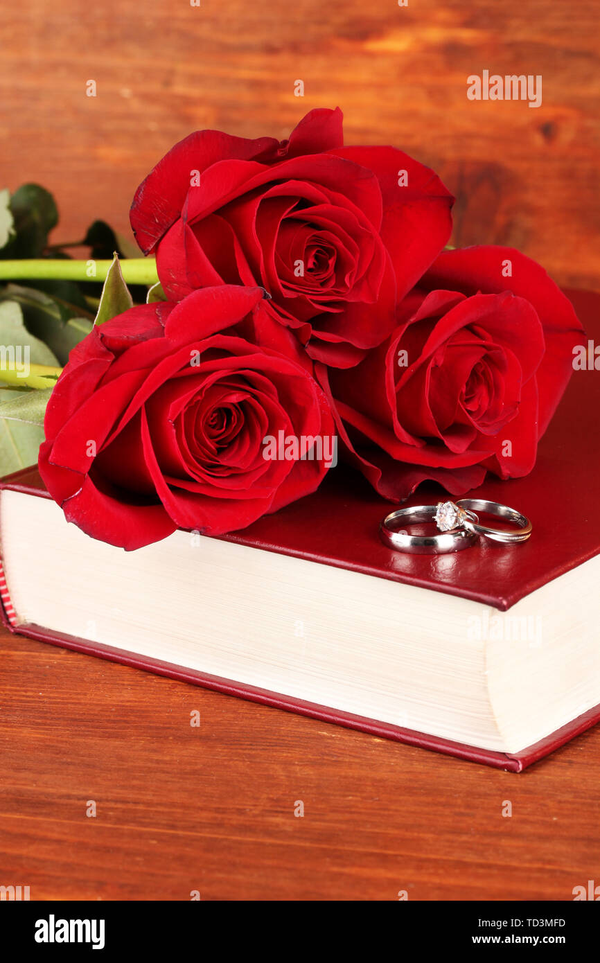 Wedding rings on bible with roses on wooden background Stock Photo