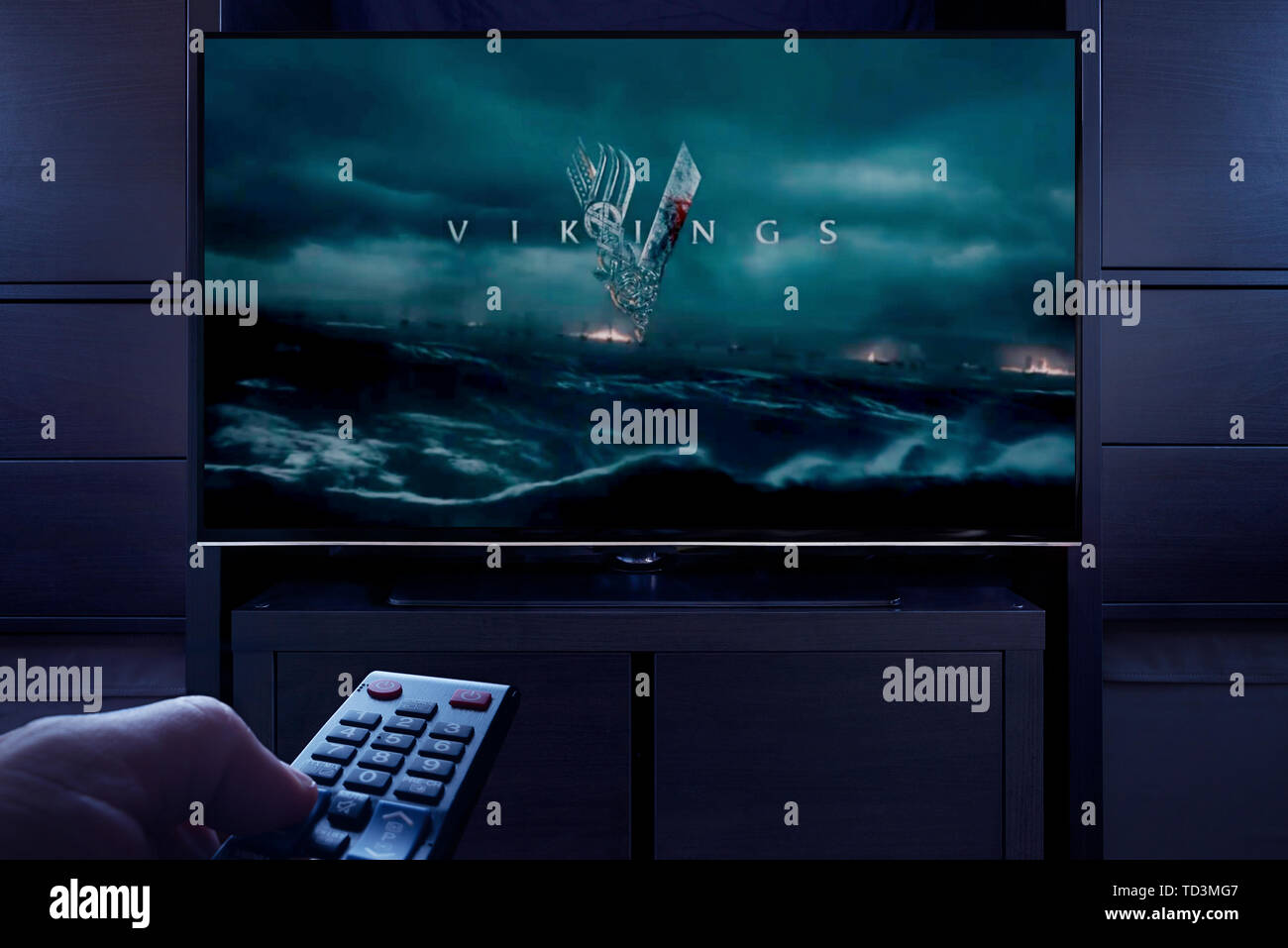 A man points a TV remote at the television which displays the Vikings main title screen (Editorial use only). Stock Photo