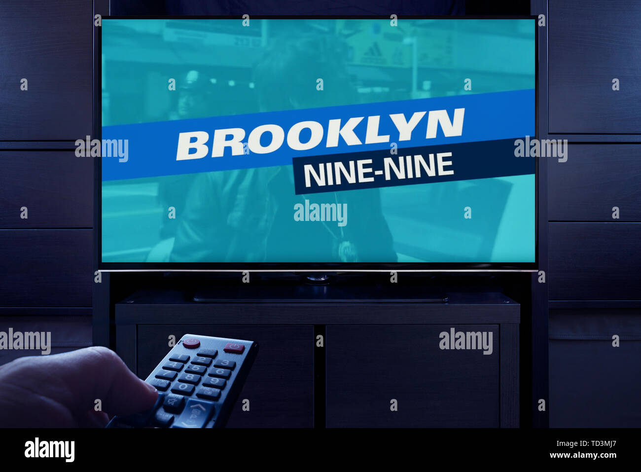 A man points a TV remote at the television which displays the Brooklyn Nine Nine main title screen (Editorial use only). Stock Photo