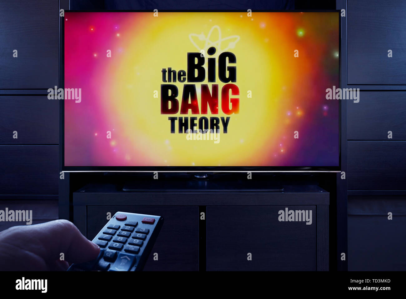 A man points a TV remote at the television which displays the Big Bang Theory main title screen (Editorial use only). Stock Photo