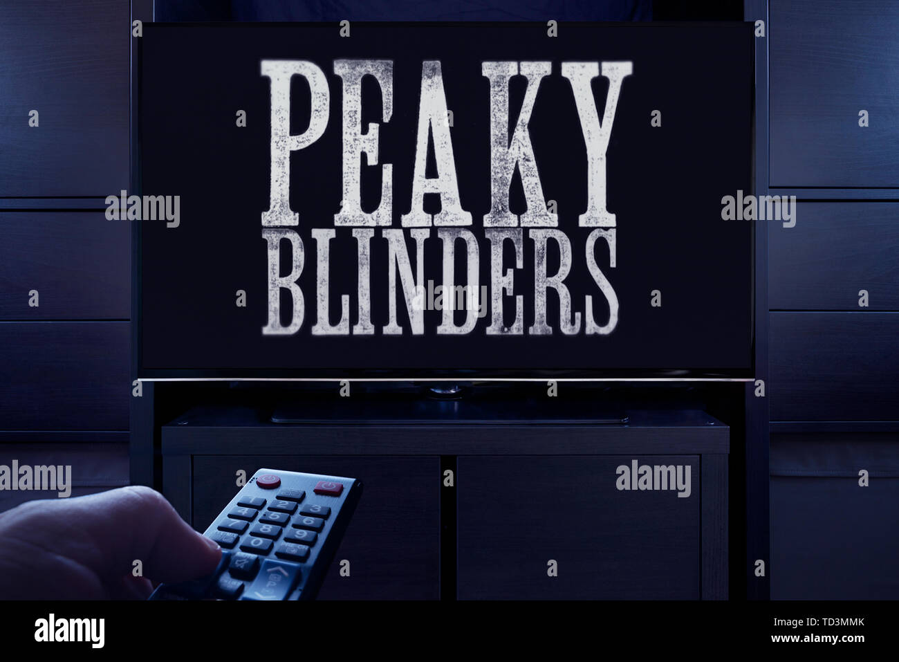 A man points a TV remote at the television which displays the Peaky Blinders main title screen (Editorial use only). Stock Photo