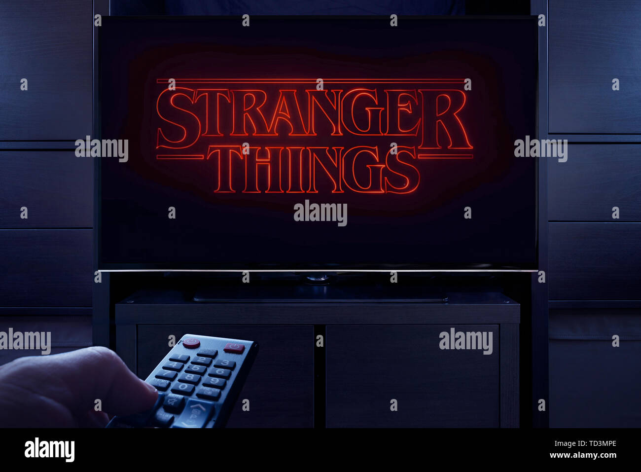 A man points a TV remote at the television which displays the Stranger Things main title screen (Editorial use only). Stock Photo