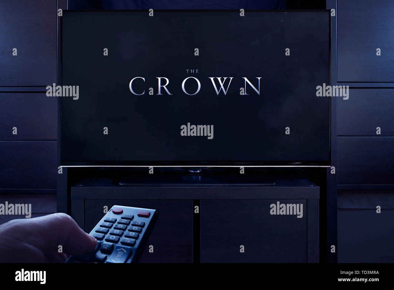 A man points a TV remote at the television which displays the Crown main title screen (Editorial use only). Stock Photo