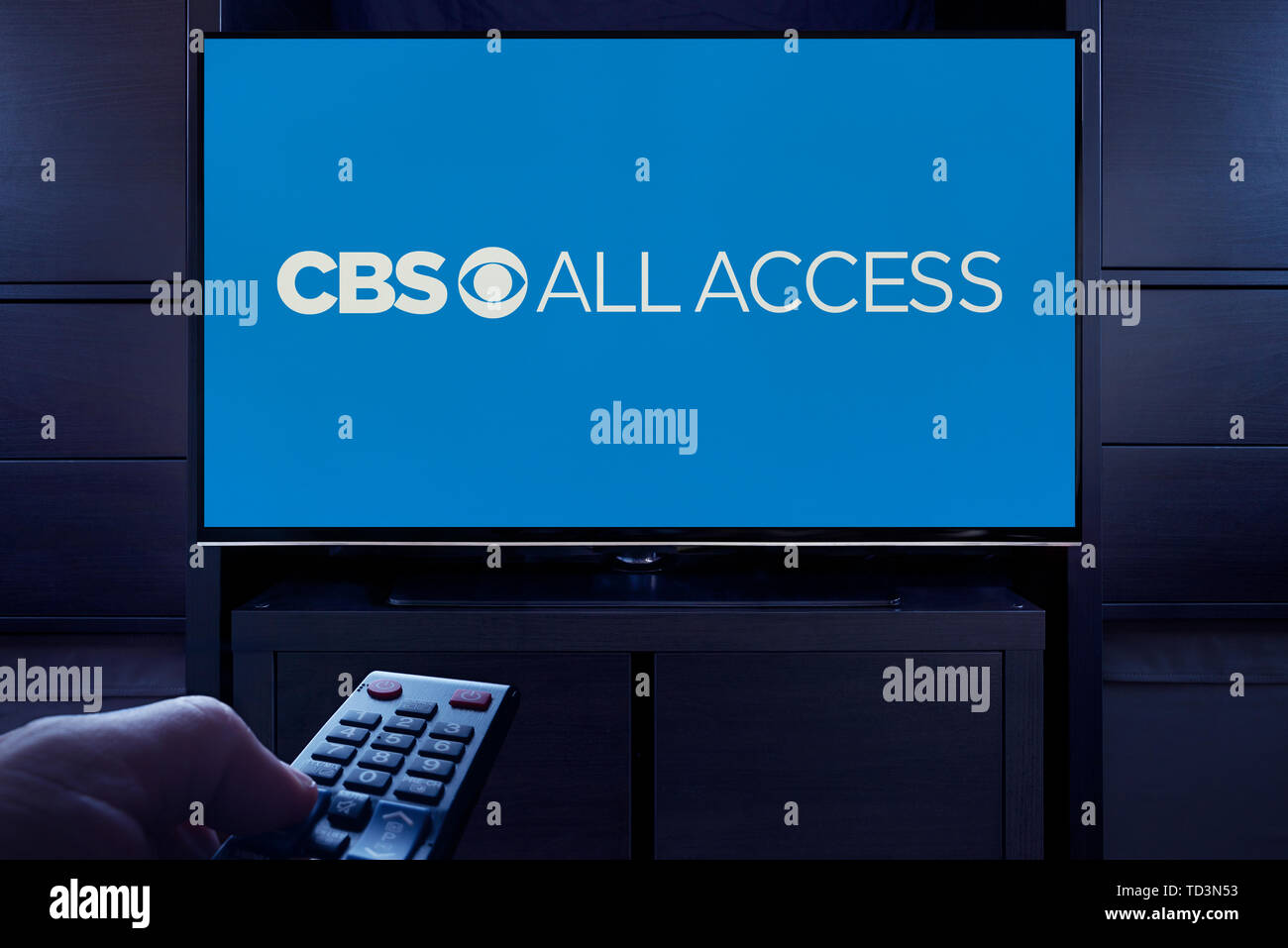A man points a TV remote at the television which displays the logo for the CBS All Access on demand video streaming service (Editorial use only). Stock Photo