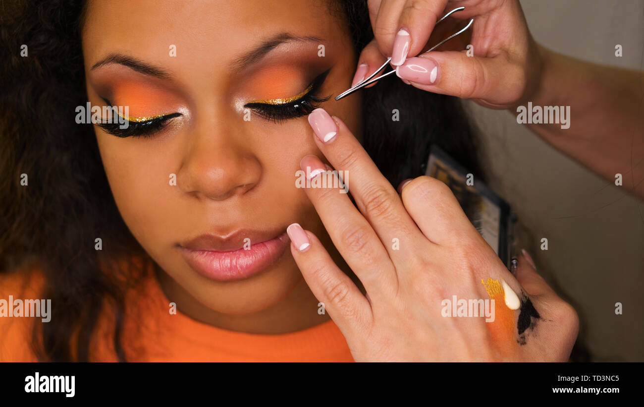 Makeup artist sticks false eyelashes of african american girl. Evening  make-up. Closeup portrait Stock Photo - Alamy
