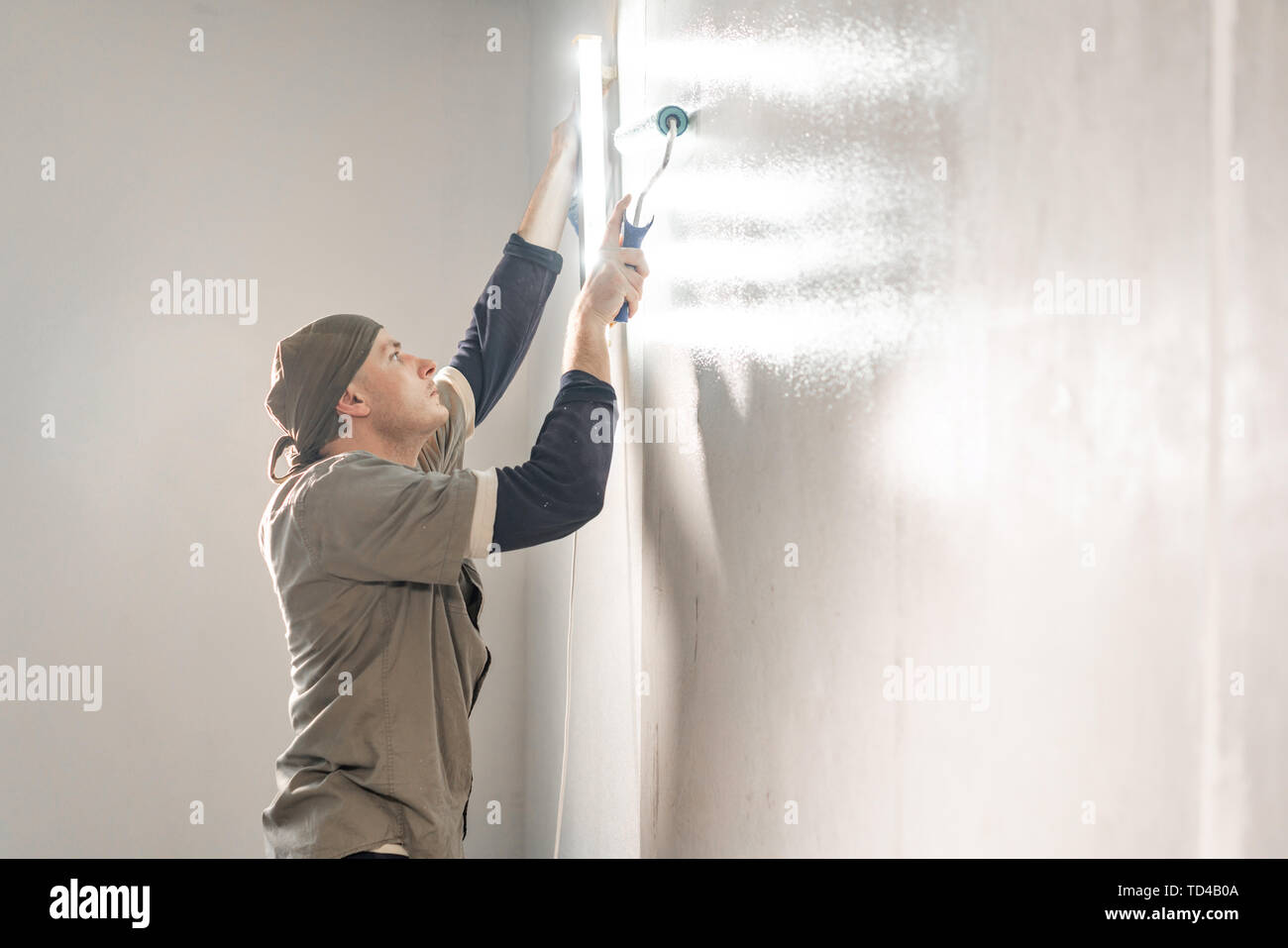Young repairman smear on wall glue with a roller. . Worker glueing