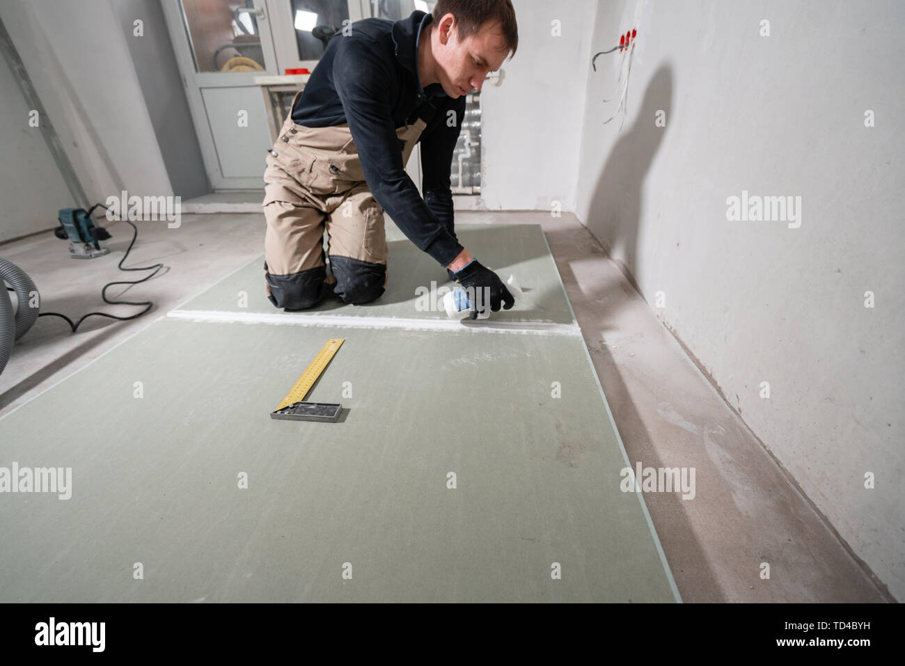 Worker is using a polyurethane foam for gluing drywall at ninety degrees. Hand holding polyurethane expanding foam glue gun applicator Stock Photo