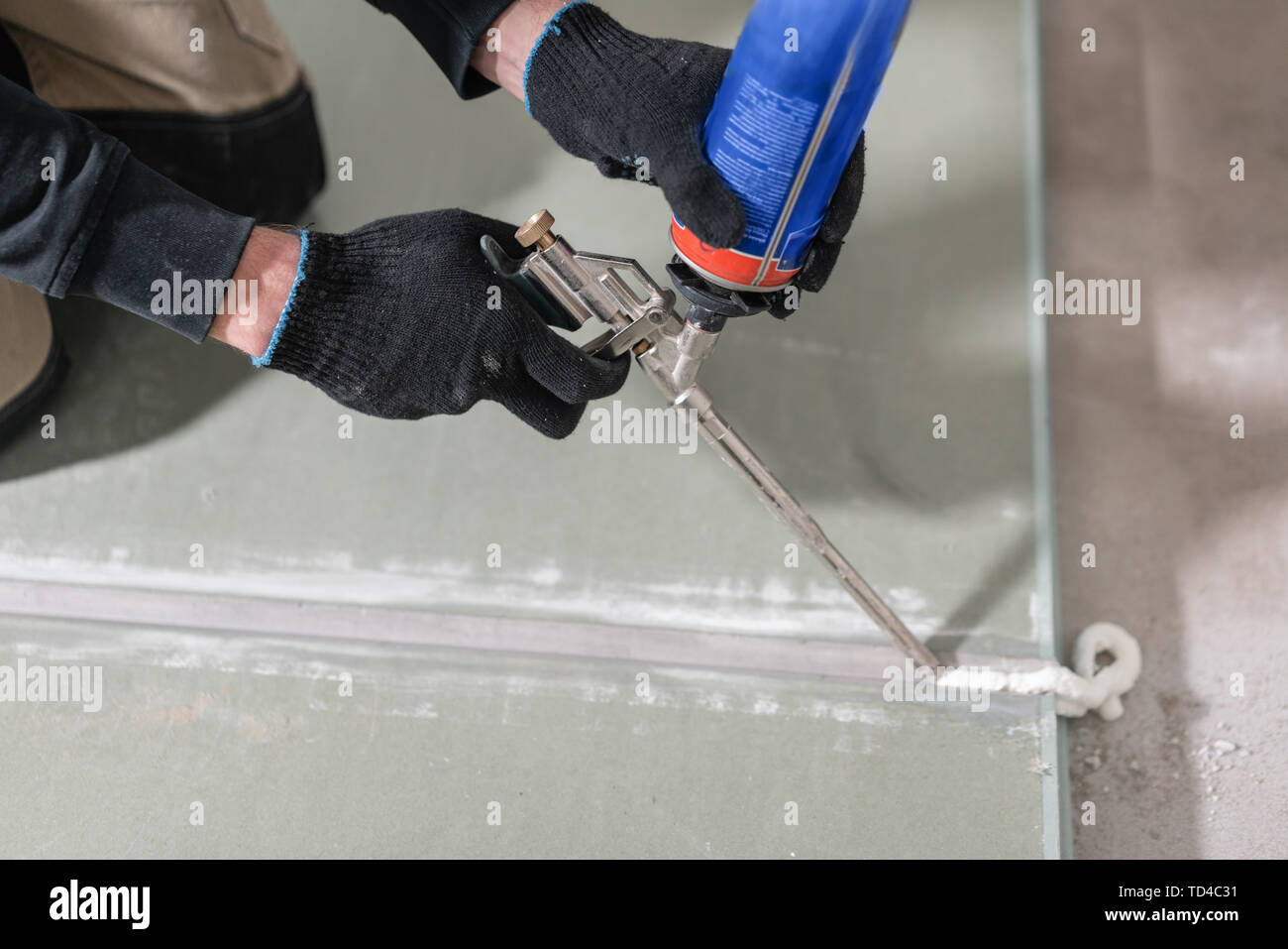 Worker is using a polyurethane foam for gluing drywall at ninety degrees. Hand holding polyurethane expanding foam glue gun applicator Stock Photo