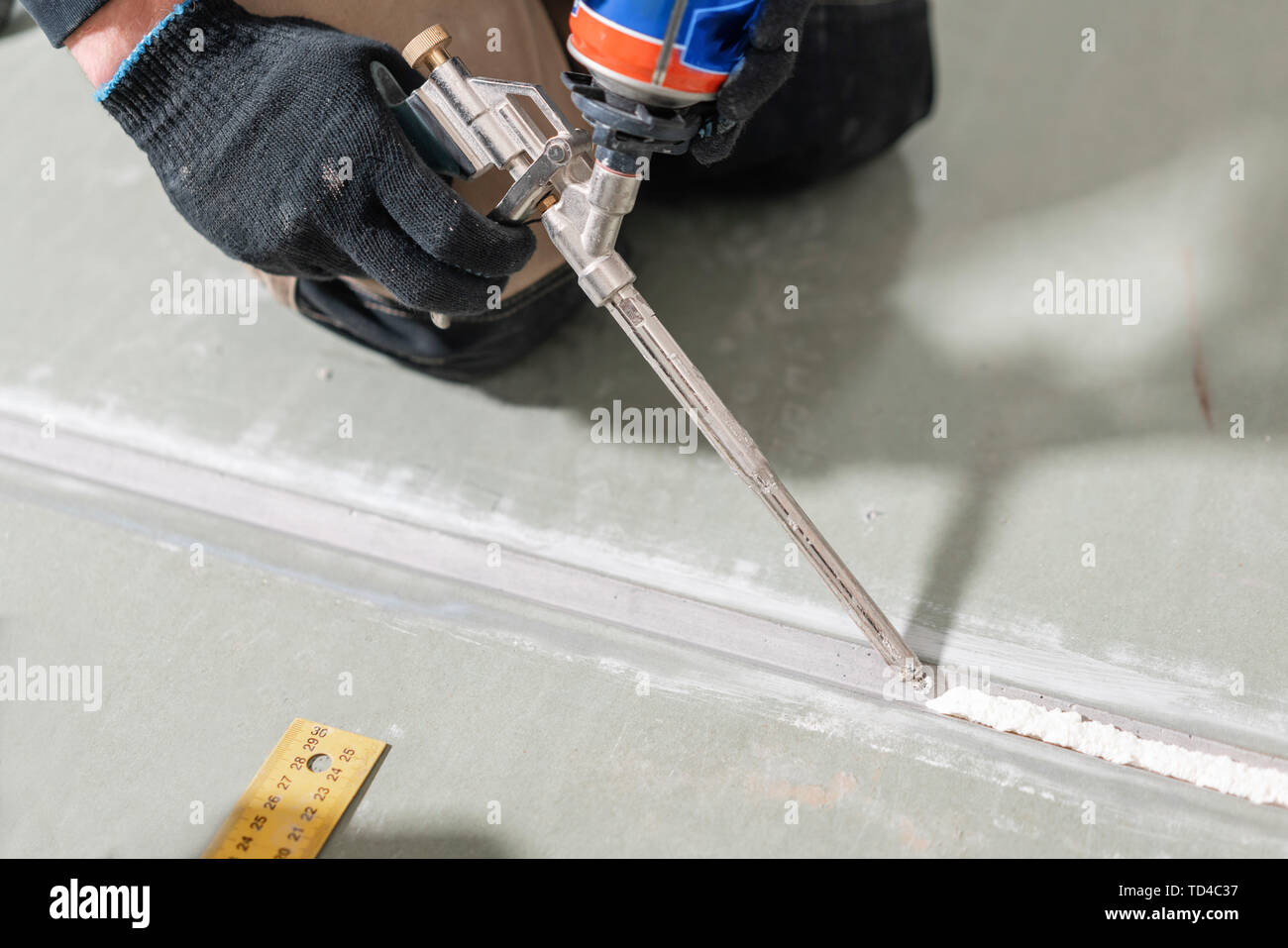 Worker is using a polyurethane foam for gluing drywall at