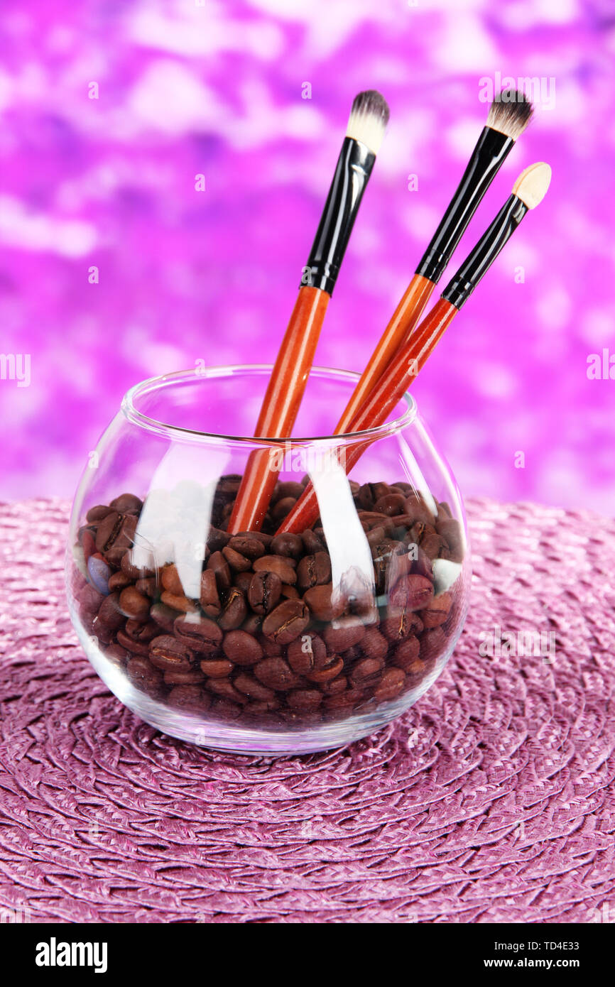 Glass bowl with coffee beans and brushes on bright background Stock