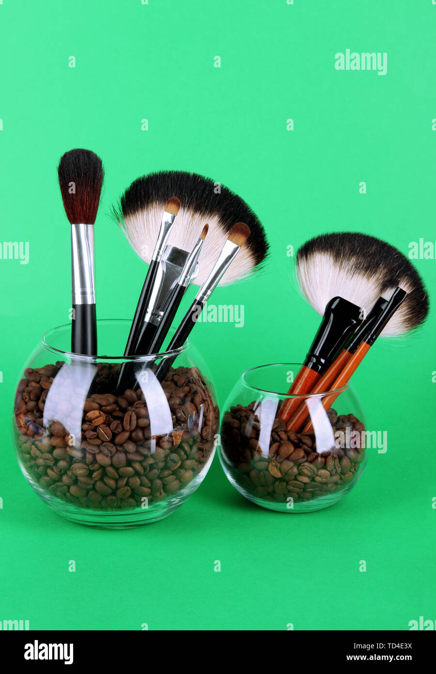 Glass bowls with coffee beans and brushes on green background Stock