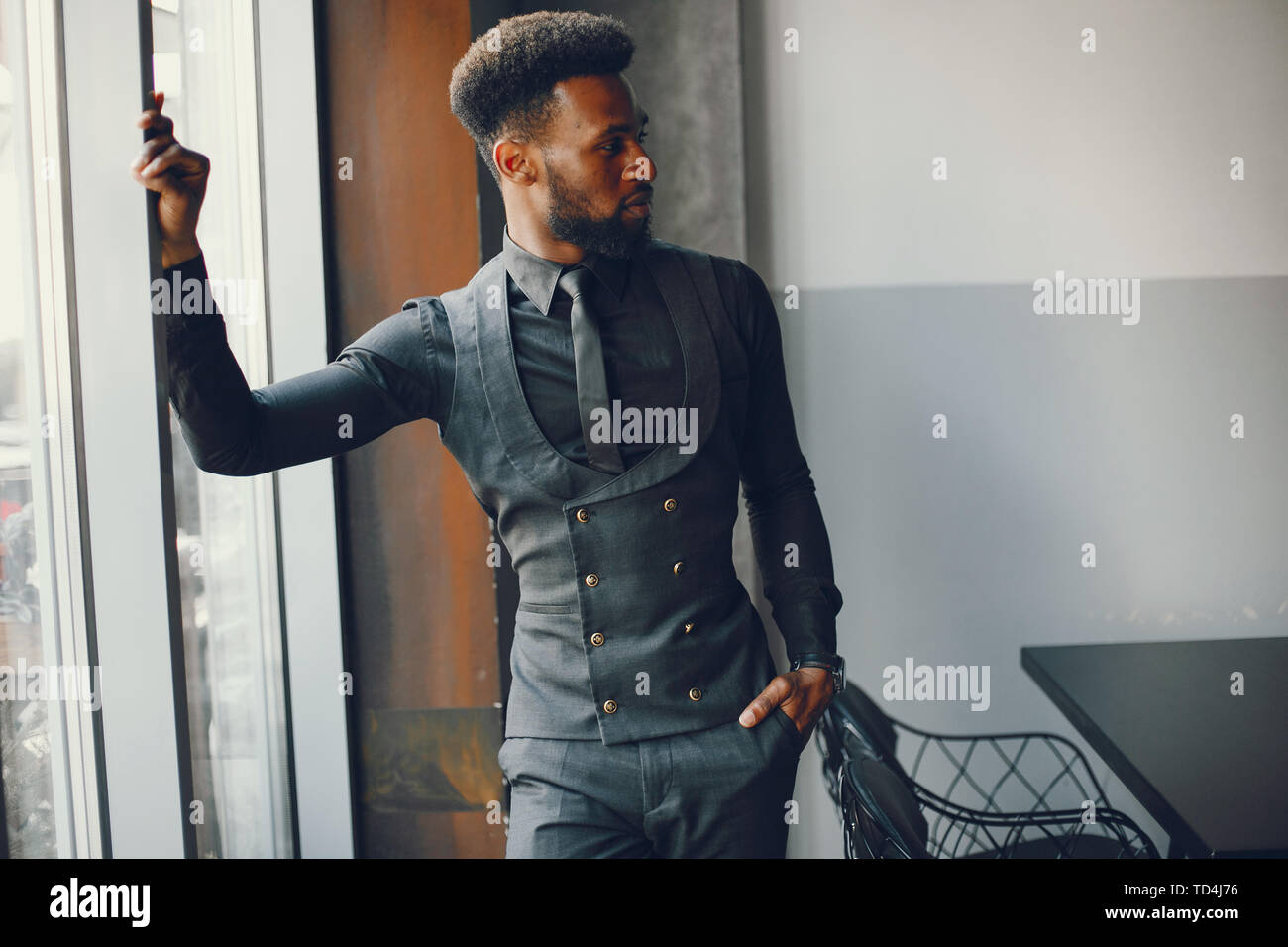 A young and handsome dark-skinned boy in a black suit standing in a cafe Stock Photo