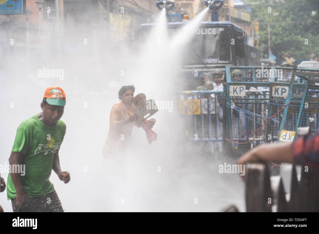 Kolkata, India. 12th June, 2019. Kolkata, India. 12th June, 2019. A Bharatiya Janata Party (BJP) supporter runs back holding a placard of Narendra Modi as police use water cannons during the protest in Kolkata. Bharatiya Janata Party workers protest against the killings of the BJP workers and also highlighting the alleged deterioration of law and order in the state, the Police used water cannons and tear gas shells towards the protesters who held a rally at Kolkata Police headquarters. Credit: SOPA Images Limited/Alamy Live News Stock Photo