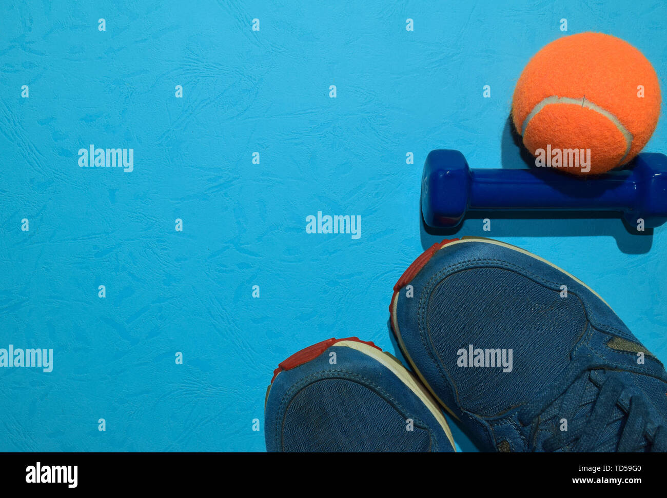 blue dumbbell, sneakers and orange tennis ball indicating workout plan on blue background. Top view with copy space for any design. Healthy and fitnes Stock Photo