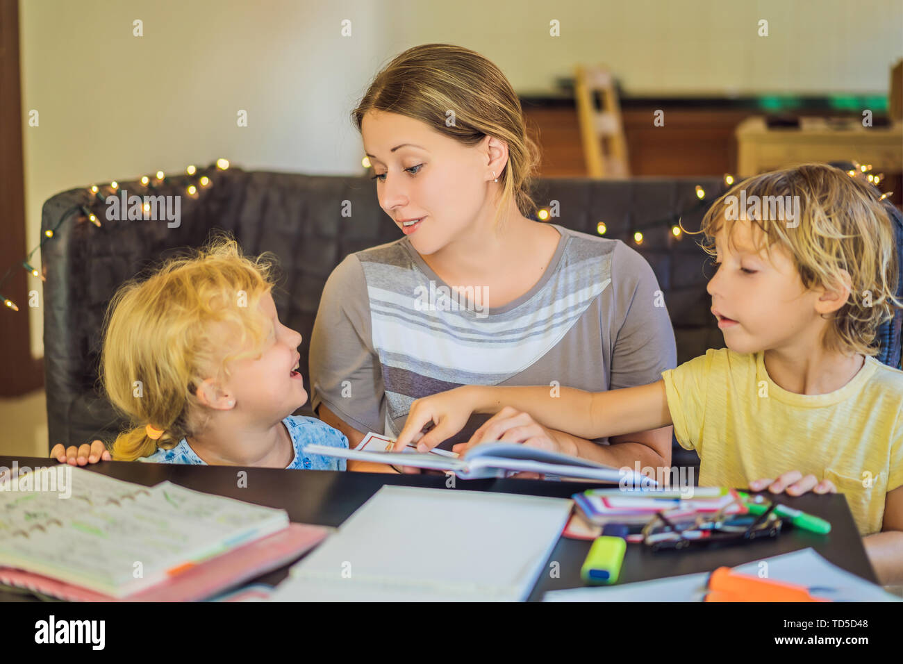 Teacher, tutor for home schooling Boy and girl at the table. Or mother, daughter and son. Homeschooling Stock Photo