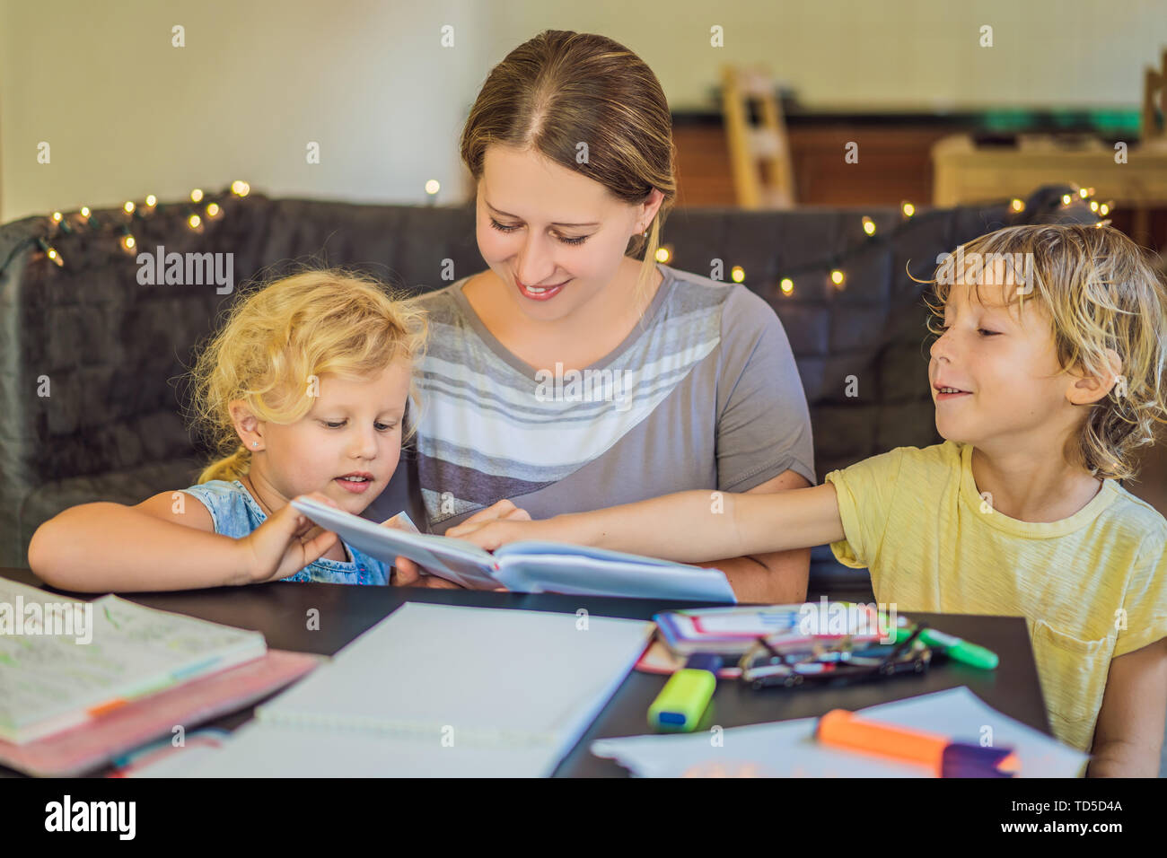 Teacher, tutor for home schooling Boy and girl at the table. Or mother, daughter and son. Homeschooling Stock Photo