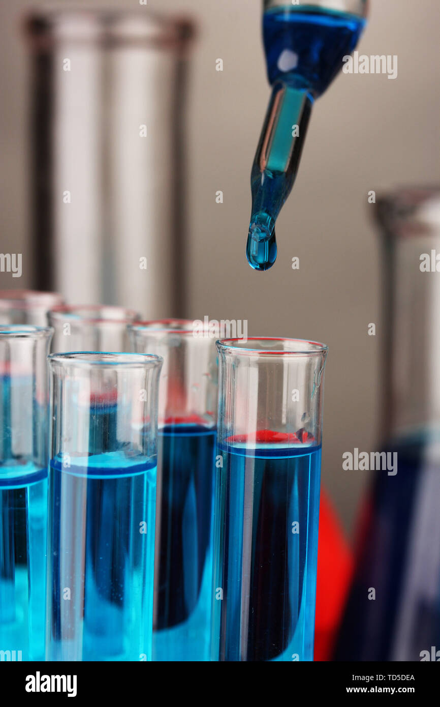 Laboratory pipette with drop of color liquid over glass test tubes ...