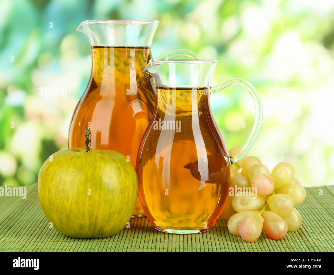Apple juice in pitchers on table on bright background Stock Photo