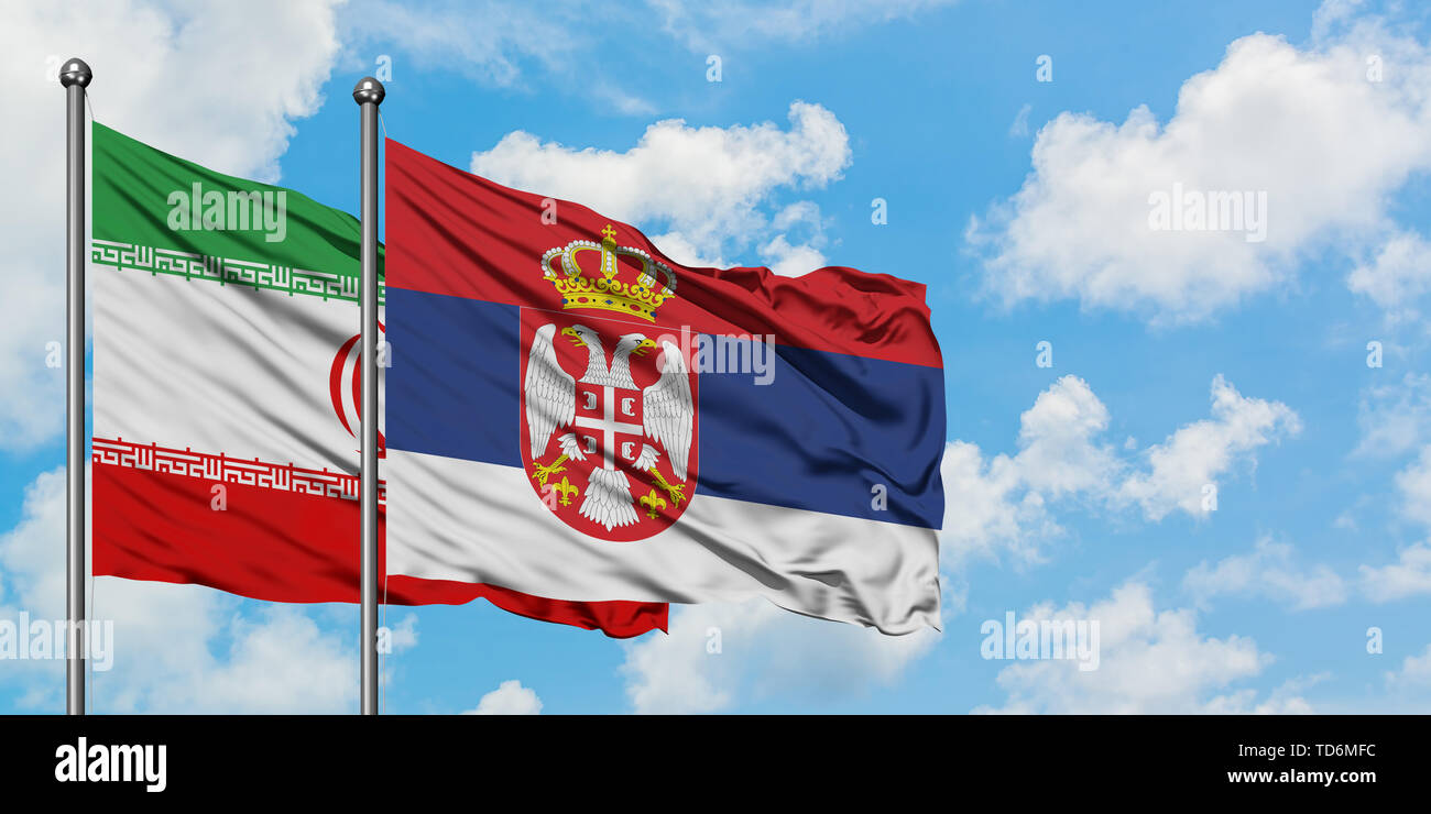 Iran and Serbia flag waving in the wind against white cloudy blue sky ...