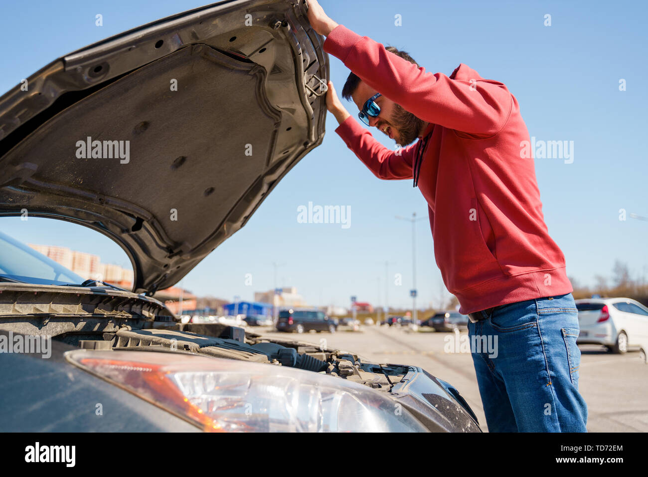Image of side of man with glasses next to open hood of broken car