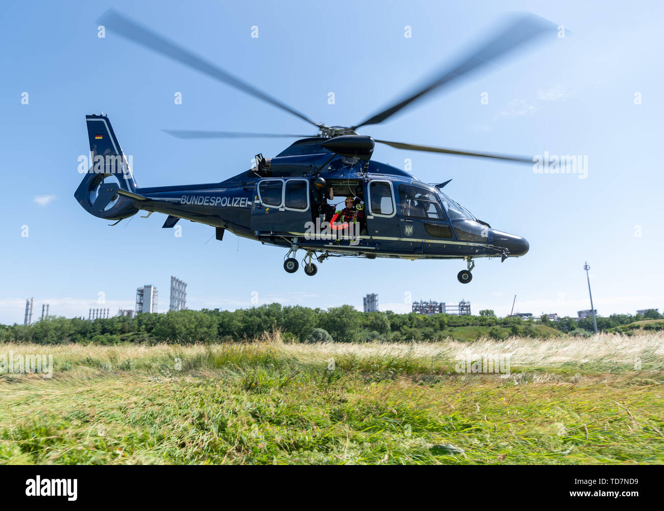 13 June 2019, Saxony, Nünchritz: An EC 155 b1 helicopter takes off from a field during a helicopter-assisted water rescue exercise from the Elbe. The Bundespolizei-Fliegerstaffel Blumberg, together with the Wasserwacht Sachsen and the Deutsche Lebens-Rettungs-Gesellschaft e.V. (German Life and Rescue Society), leads the (DLRG) is conducting a joint exercise to rescue people from flowing waters. The Wacker Chemie AG plant can be seen in the background. Photo: Robert Michael/dpa-Zentralbild/dpa Stock Photo