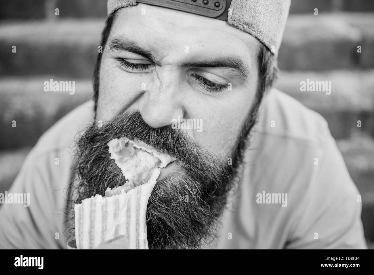 Unleashed appetite. Street food concept. Man bearded eat tasty sausage. Urban lifestyle nutrition. Carefree hipster eat junk food while sit stairs. Guy eating hot dog. Junk food. Snack for good mood. Stock Photo