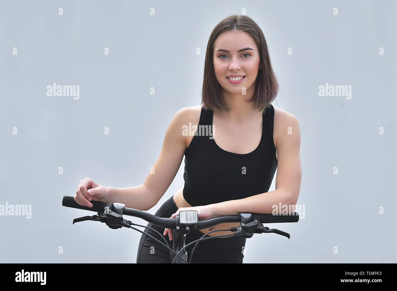 Smiling beautiful young girl standing with her bicycle on the street. City scene. Warm summer day. Stock Photo