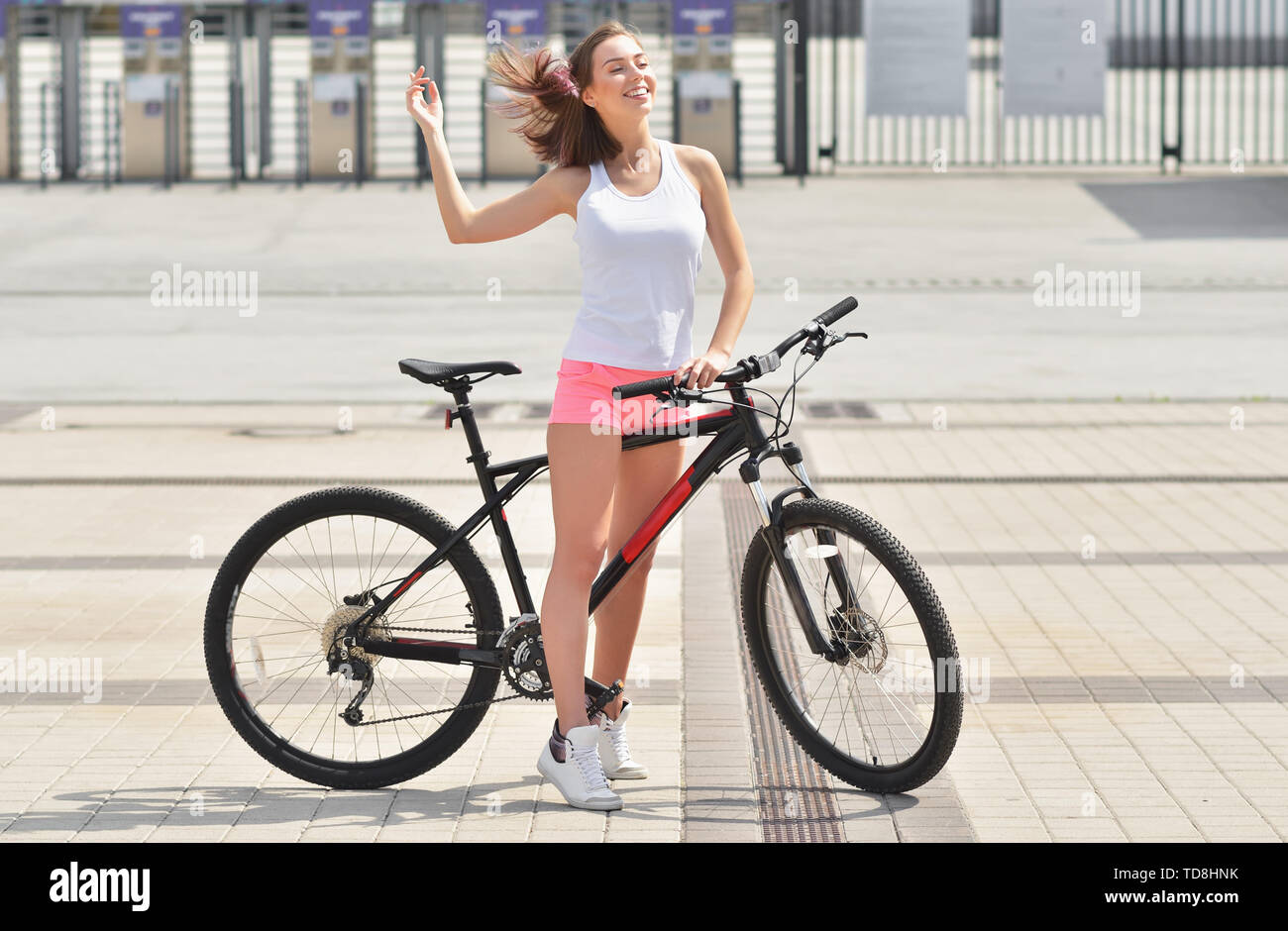 Young beautiful hipster woman in white dress and pink shorts, summer trend style, riding bicycle, travel. City, slim, tanned skin, positive, close-up  Stock Photo