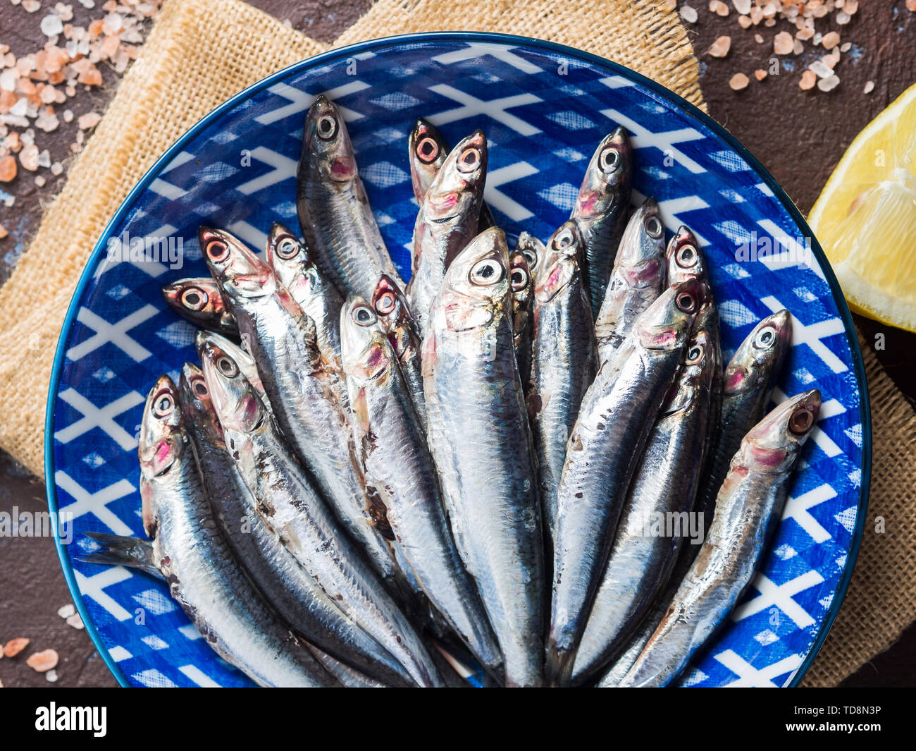 Blue fish. Fresh anchovies in a dish with pink salt and lemon on dark background. Healthy protein meal. Local seafood, Italy Stock Photo