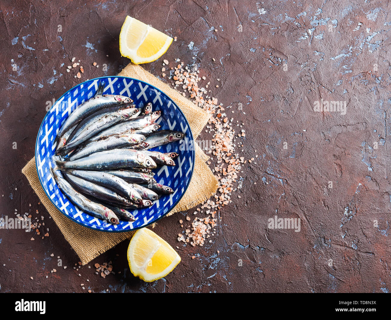 Blue fish. Fresh anchovies in a dish with pink salt and lemon on dark