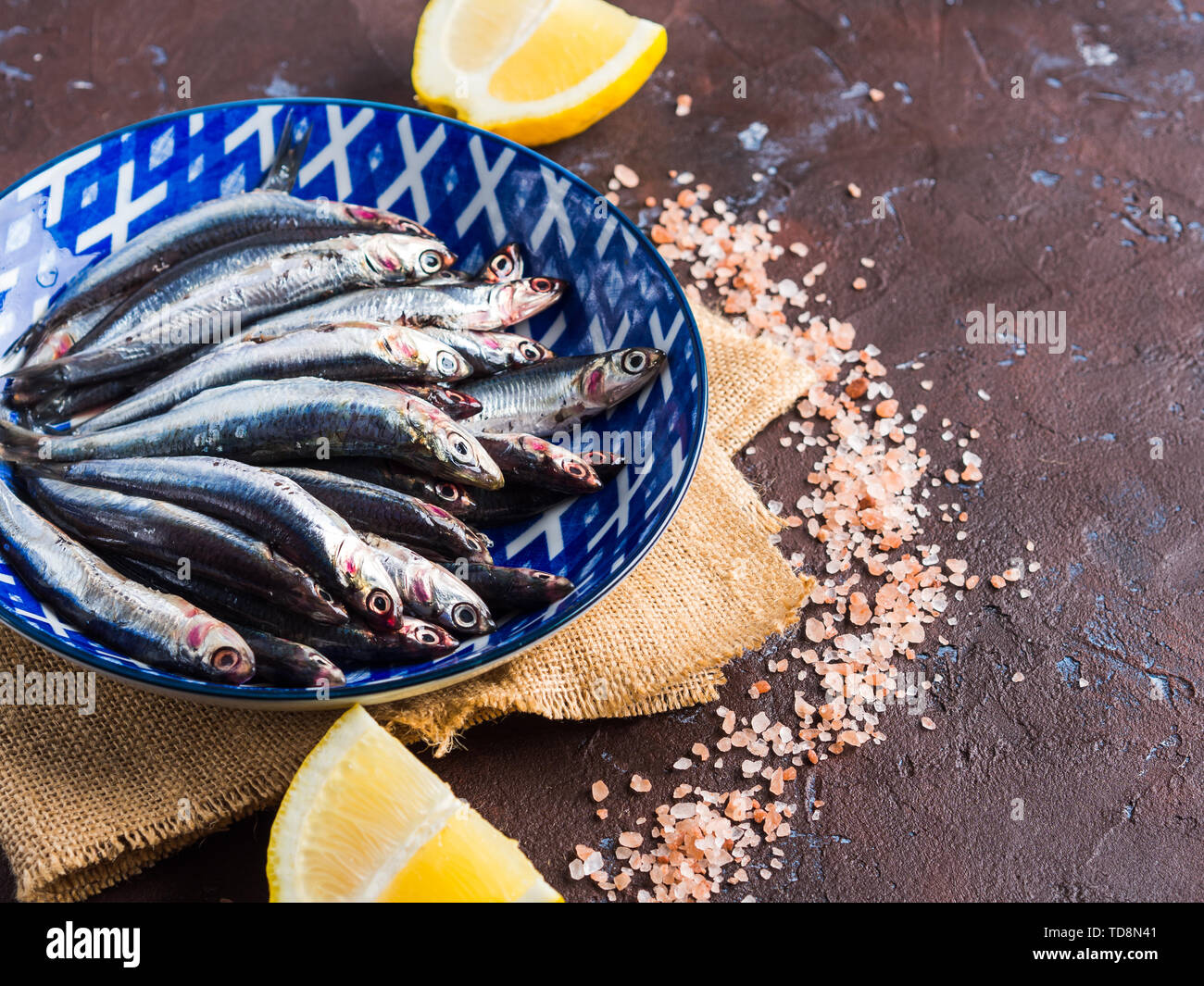 Blue fish. Fresh anchovies in a dish with pink salt and lemon on dark