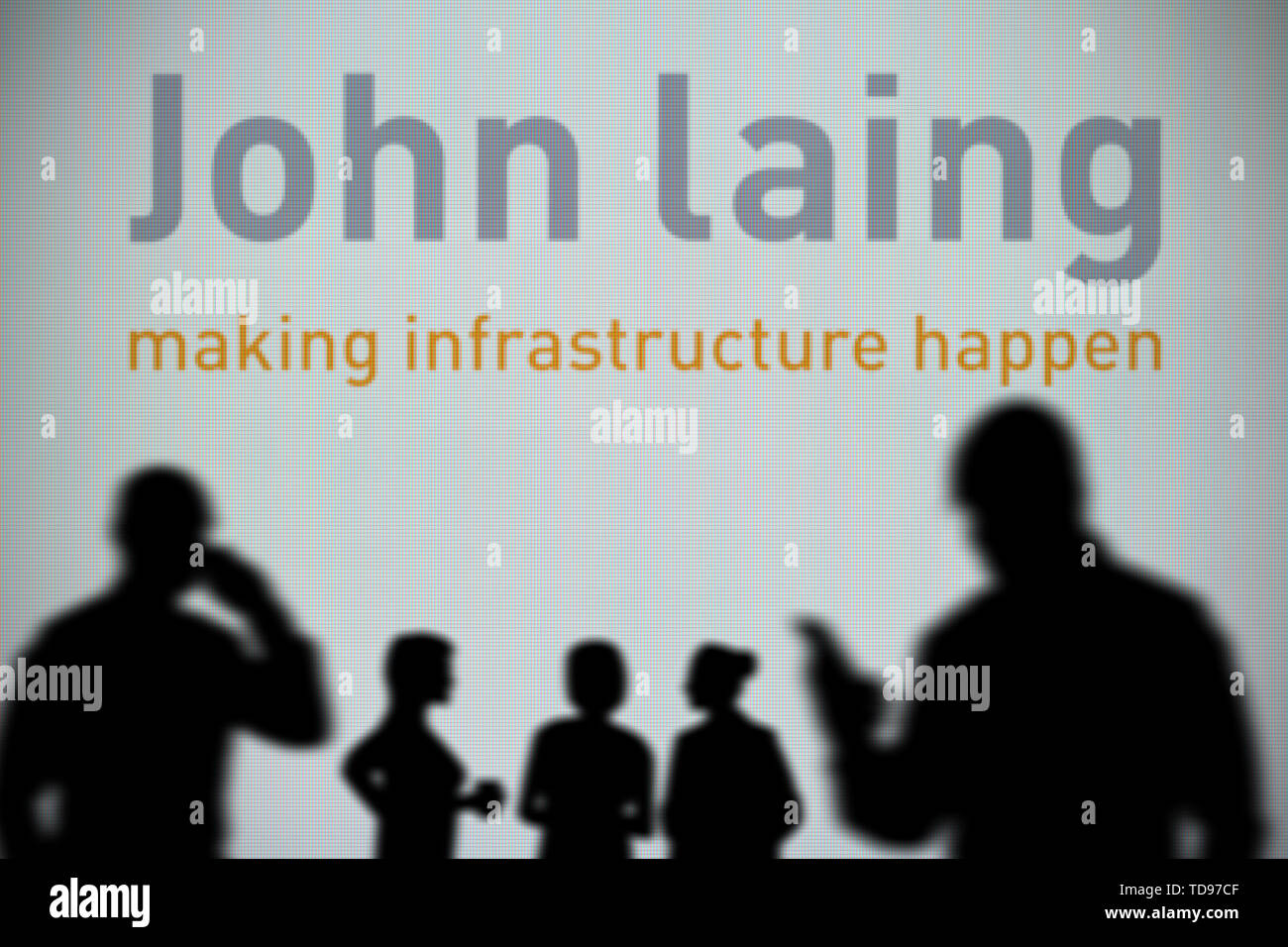 The John Laing logo is seen on an LED screen in the background while a silhouetted person uses a smartphone in the foreground (Editorial use only) Stock Photo