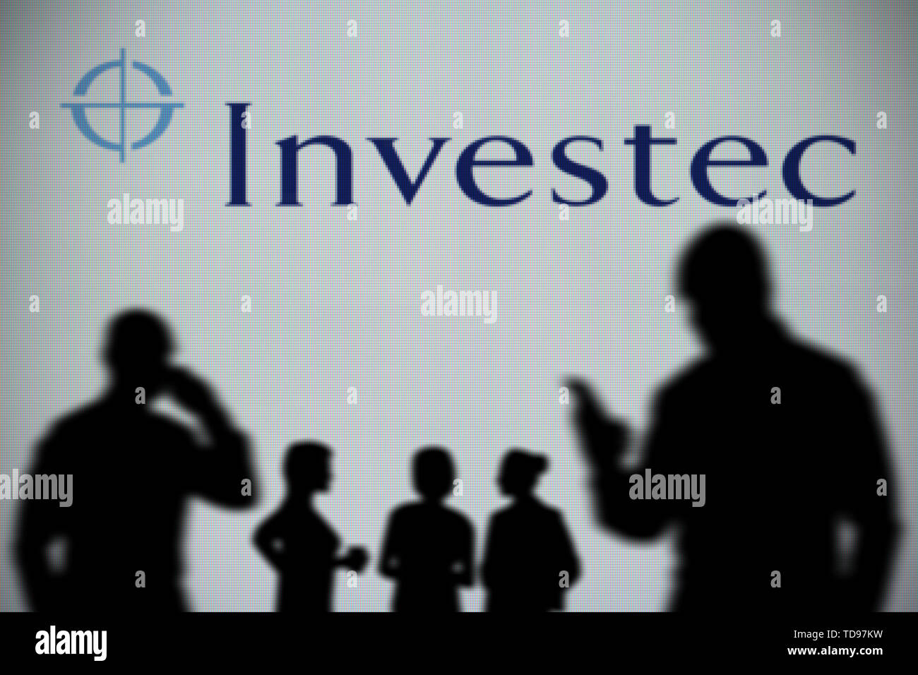 The Investec logo is seen on an LED screen in the background while a silhouetted person uses a smartphone in the foreground (Editorial use only) Stock Photo