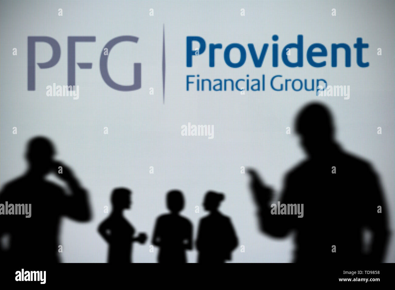 The Provident Financial Group (PFG) logo is seen on an LED screen in the background while a silhouetted person uses a smartphone (Editorial use only) Stock Photo