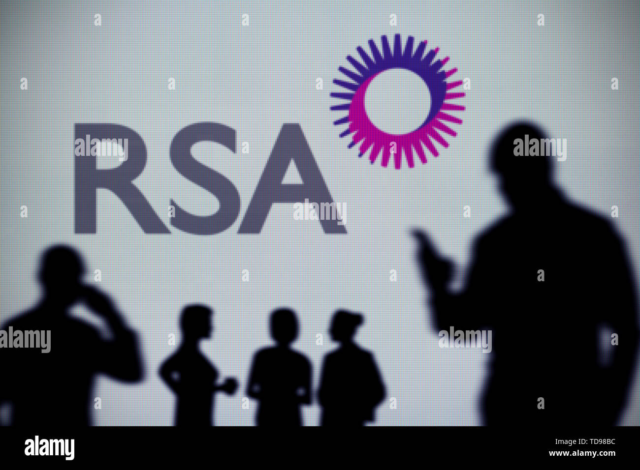 The Royal Sun Alliance (RSA) logo is seen on an LED screen in the background while a silhouetted person uses a smartphone (Editorial use only) Stock Photo