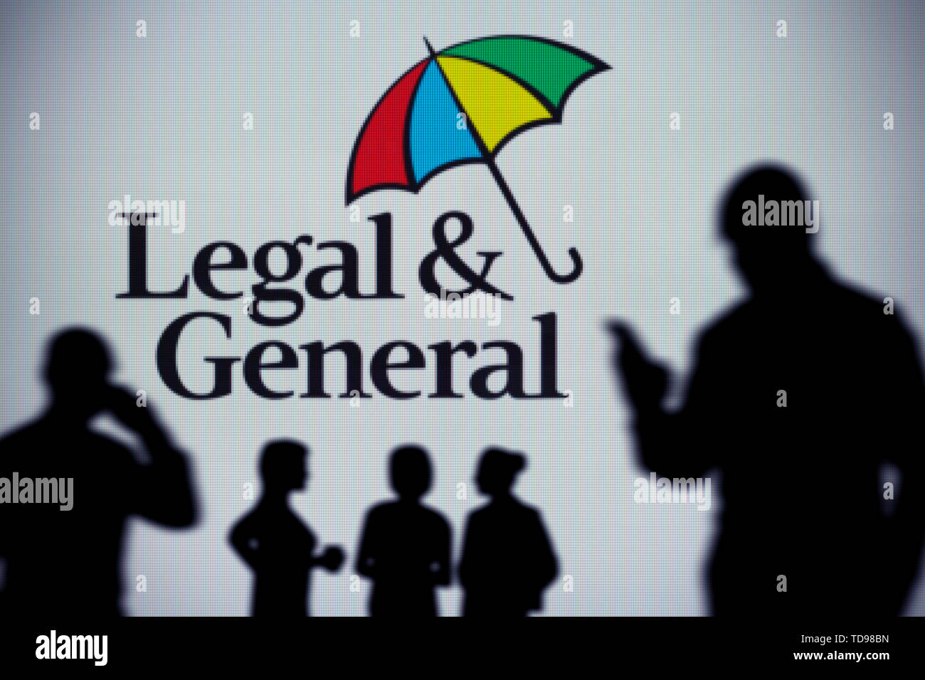The Legal and General logo is seen on an LED screen in the background while a silhouetted person uses a smartphone (Editorial use only). Stock Photo