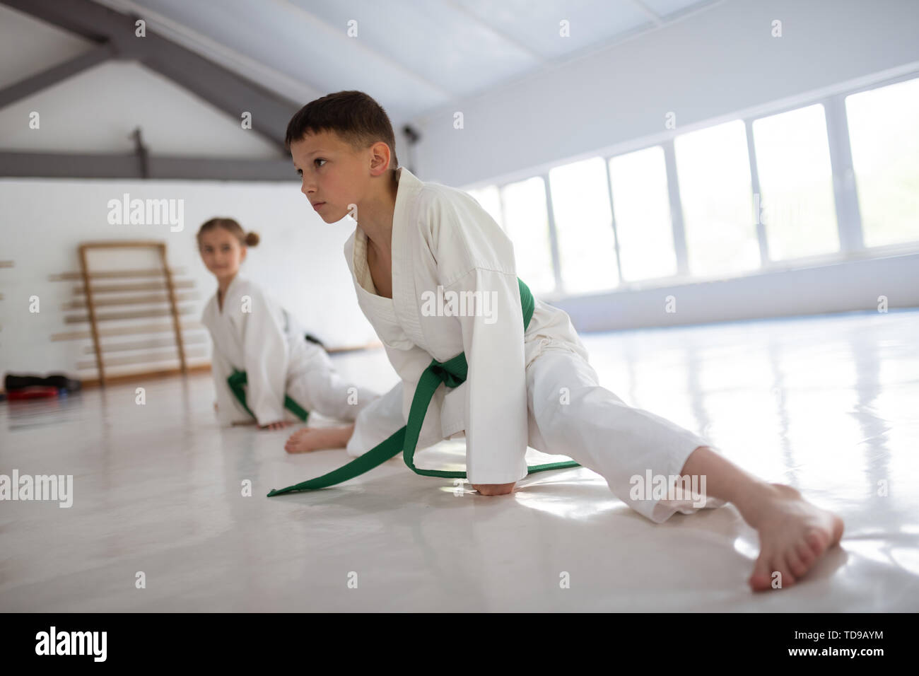 Boy making split. Dark-haired boy making leg split while stretching legs before aikido Stock Photo