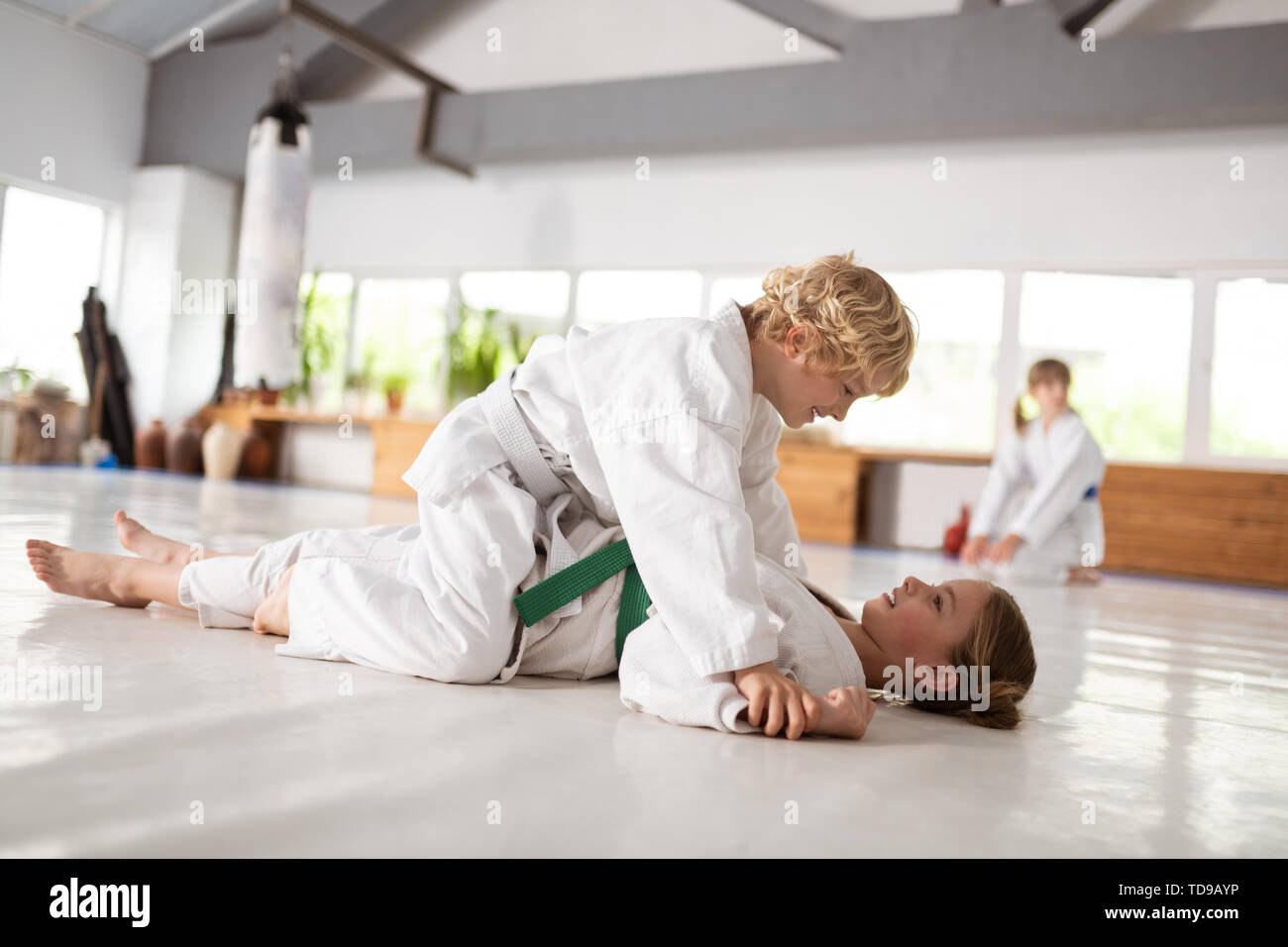 Boy winning. Blonde-haired boy sitting on girl after winning aikido fight with her Stock Photo