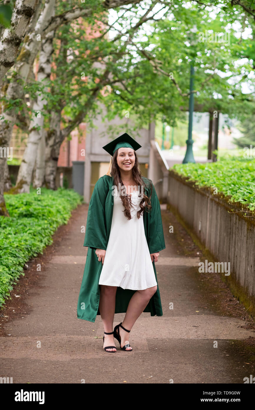 University graduate on her college campus in a cap and gown celebrating graduating from her undergrad bachelor's degree during the Spring. Stock Photo