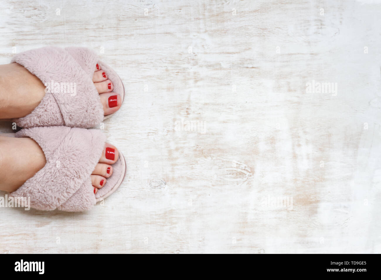 female legs with red nails in home fur fluffy pink slippers on a light wooden background. flat lay. Top view. The concept of a cozy bright girl house. Stock Photo
