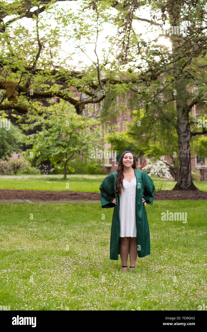 University graduate on her college campus in a cap and gown celebrating graduating from her undergrad bachelor's degree during the Spring. Stock Photo