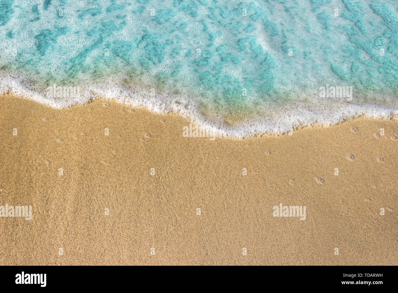 Soft blue waves with foam of ocean on the sandy beach background. Stock Photo